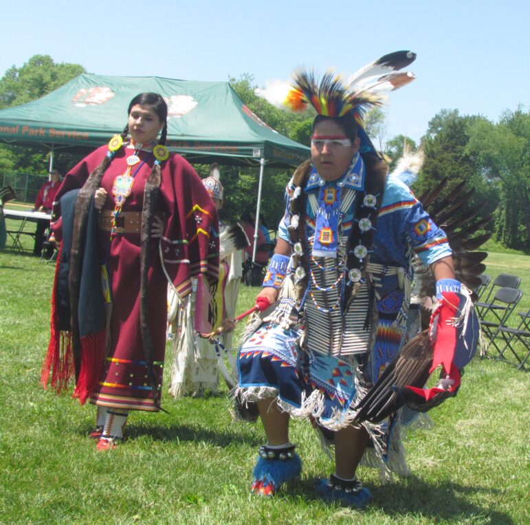 Native American man and woman dancing in traditional powwow regalia at a Running Strong event on a sunny day.