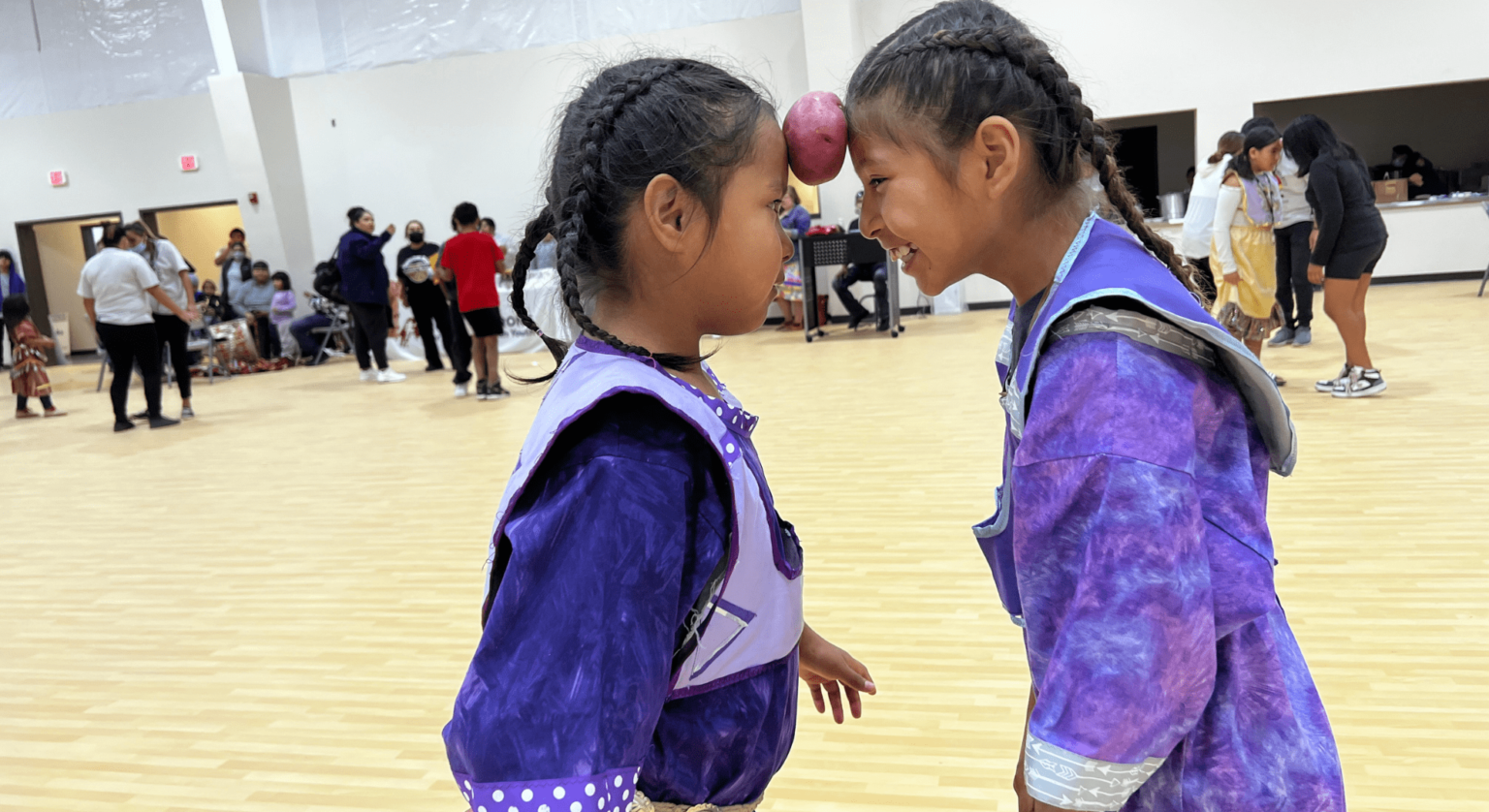 Two young Oglala Lakota girls smiling and touching foreheads at the Oyate Ta Kola Ku Community Center on the Pine Ridge Reservation
