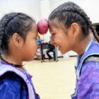 Two girls playing a game with a potato pushed against their foreheads smiling and not worrying about pine ridge reservation poverty.