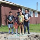 A Native American family smiles next to a new red water pump, providing clean water access from the Mni Wiconi program.