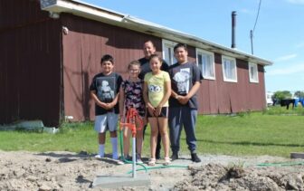 A Native American family smiles next to a new red water pump, providing clean water access from the Mni Wiconi program.