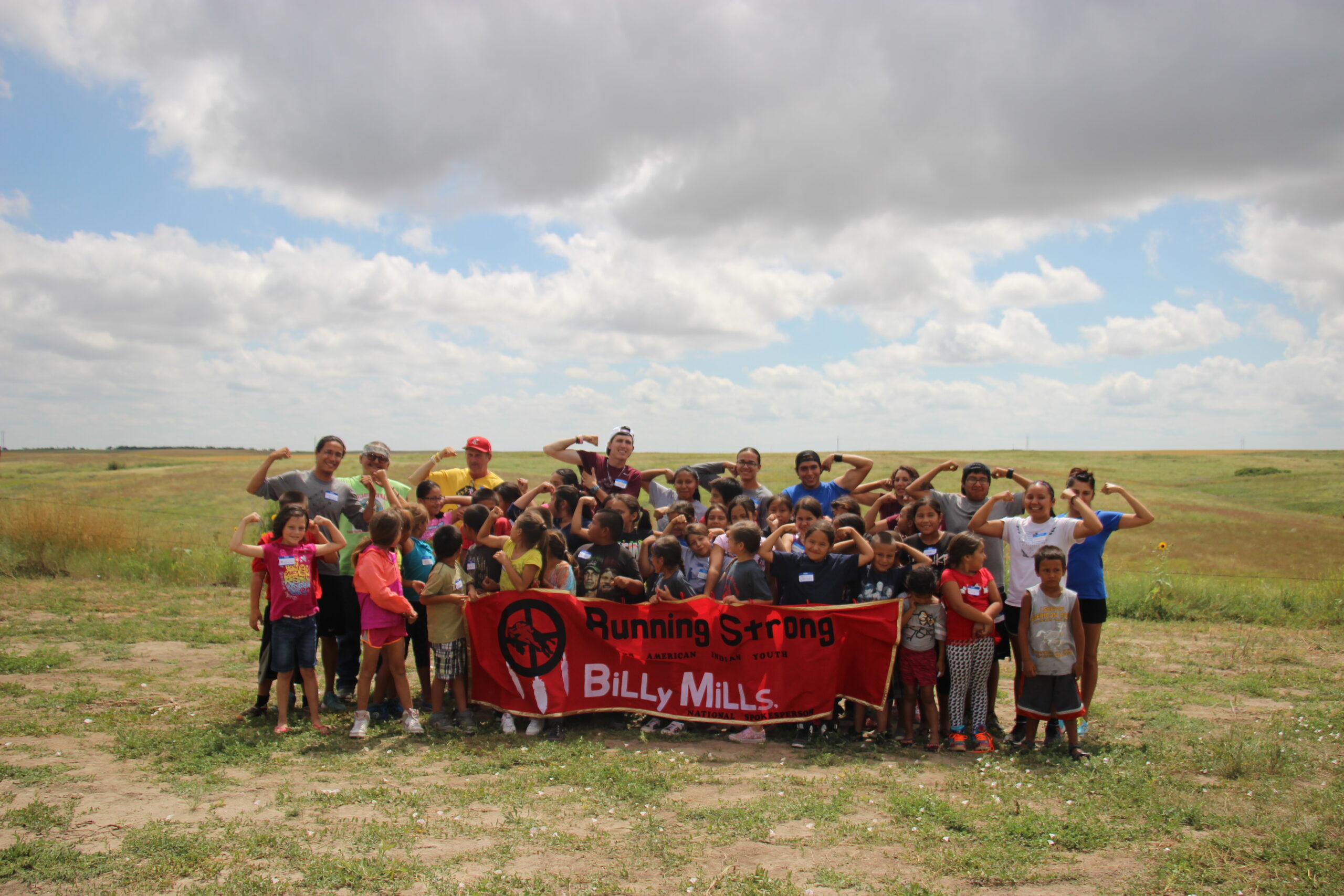 A group of youth in a field is having fun and holding up a banner.