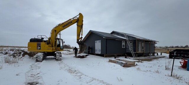 An excavator next to a home with solar panels, installing sustainable tech for a tribal energy sovereignty project.