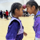 Two girls smiling as they balance a potato between their foreheads while doing the potato dance at a community center activity.