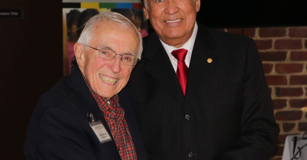 Billy Mills and Gene Krizek smiling and holding hands.