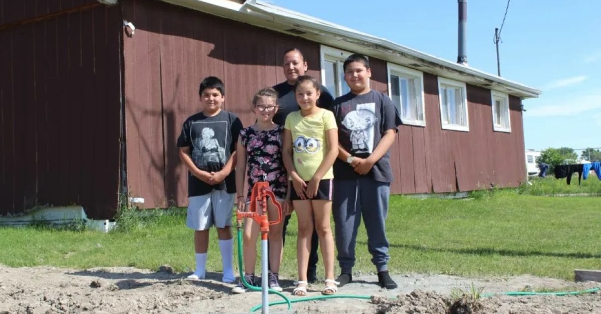 A Native American family smiles next to a new red water pump, providing clean water access from the Mni Wiconi program.